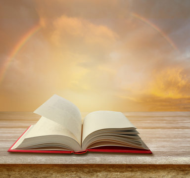 open pages of book on table in front of rainbow sky