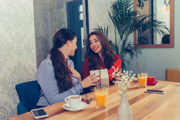 Young beautiful girl sitting in cafe with her friend and receiving a gift