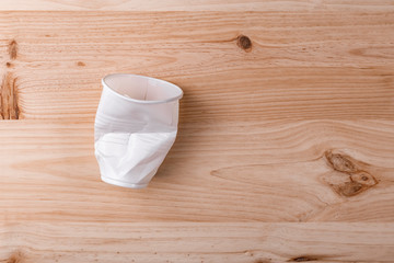 Broken crumpled white plastic Cup lies on a wooden table of natural color
