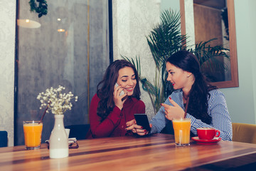 Two young women drinking coffee and using phone in cafe