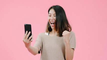 Naklejka premium Young Asian woman using smartphone checking social media feeling happy smiling in casual clothing over pink background. Happy smiling adorable glad woman rejoices success.
