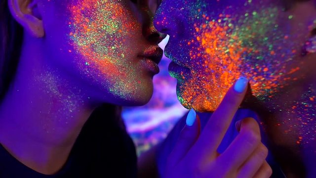 Couple kissing in the disco club with fluorescent paintings on the faces