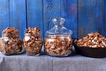 Homemade granola with different nuts and seeds in three glass jars and one cast iron pan in a row