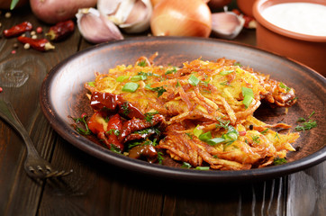 Homemade tasty potato pancakes in clay dish with sun-dried tomatoes and sour cream