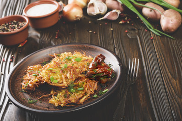 Homemade tasty potato pancakes in clay dish with sun-dried tomatoes and sour cream