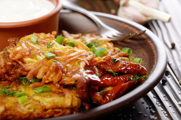 Closeup view at Homemade tasty potato pancakes in clay dish with sun-dried tomatoes and sour creram