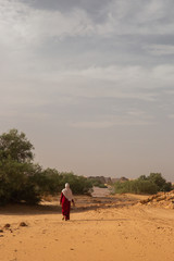 A muslim girl with hijab walking under the sun in Sahara, Algeria