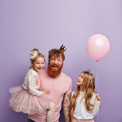 Vertical shot of overemotive joyful single dad and two daughters, celebrate Fathers Day, wear...