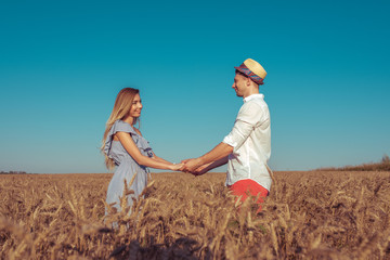 Happy young couple man woman summer wheat field, holding hands. Concept romance dating, love and care, family support and honeymoon. Emotions of joy, smiles, pleasure and outdoor recreation.