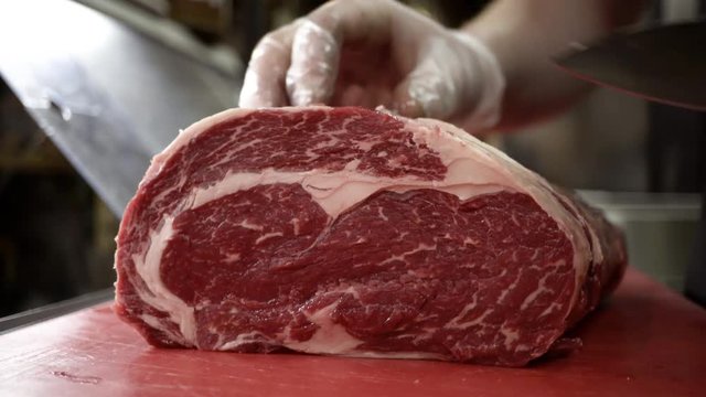 Butcher in gloves cuts carcass of red meat. Action. Close-up of professional knife cutting huge piece of meat in butcher shop