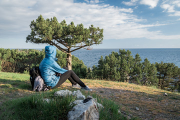 Naklejka na ściany i meble Foros, Republic of Crimea - April 1, 2019: Tourist sitting on the grass near a tree opposite the Black Sea on the southern coast of the Crimea peninsula