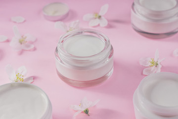 Obraz na płótnie Canvas Skin care beauty creams for the face with blooming flowers on pink background.