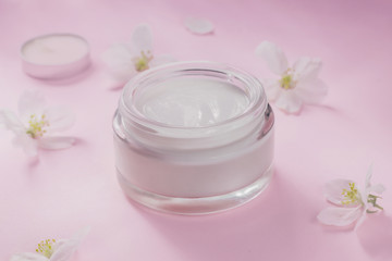 Obraz na płótnie Canvas Cream for skin care with a visible texture with a blooming flowers on pink background.