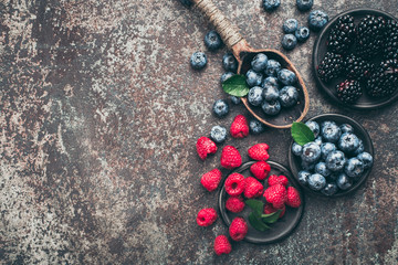 Fresh berries with raspberries, blueberries, blackberries in bowl on a stone stand on a dark metal background.