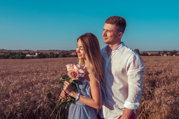 Happy young couple man woman summer wheat field with bouquet rose flowers. Concept romance dating, love care, family support honeymoon. Emotions of joy, smiles, pleasure outdoor recreation.