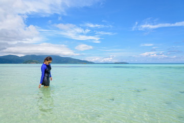 Asian woman in blue swimwear and sunglasses walking in the sea and beach looking at the clear water in summer sky at Ko Ra Wi, travel to Koh Lipe island, Tarutao National Park, Thailand