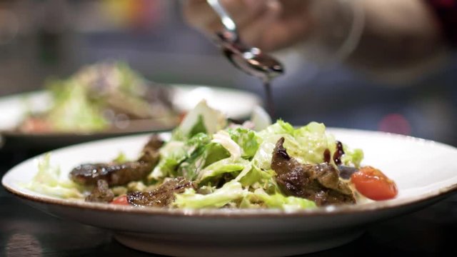 Spoon with sauce is poured over salad. Action. Closeup of aesthetic pouring jets of salad sauce by professional chef in restaurant