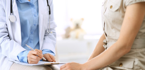 Doctor and patient talking. Physician at work in hospital while writing up medication history records form on clipboard near sitting woman. Healthcare and medicine concepts