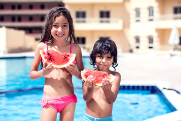 Little boy and girl eat watermelon at the swimming pool. Children and summer concept