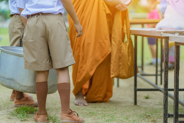 Teachers and students together make merit to give food offerings to a Buddhist monk on important religious days at school.