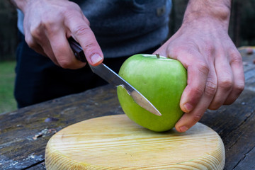 cutting with a knife a green apple on a wooden board