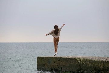 happy young girl with curly hair dancing and jumping on the sea