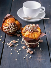 Delicious vanilla muffin with milk chocolate and nuts and a white cup on a wooden background. Close-up