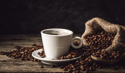 Coffee cup with coffee beans on wood background.