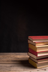 Piles of books on wooden table among black background. Education, preparing exams. Copy space