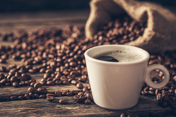 Coffee cup with coffee beans on wood background.