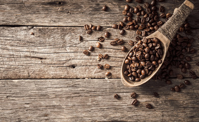 Coffee beans in wooden spoon on wood background.