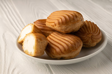 Profiteroles with whipped cream in a white plate on a wooden table
