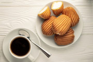 Top view of a plate with profiteroles and a cup of coffee on a white wooden table