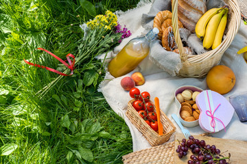 picnic on green grass. Basket with bread and a bottle and bananas in a basket and tomatoes with apples. still life on green grass. products on a picnic blanket on a summer day. place for copy space