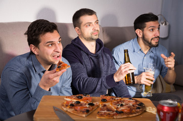 Males in suspense watching tv with beer and pizza