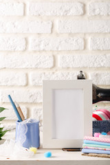 Mock up white frame on the white brick walls background, vintage sewing machines and stacks of textiles. Loft interior