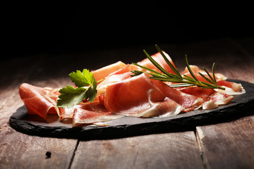 Italian prosciutto crudo or jamon with rosemary. Raw ham on wooden board