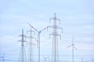 Electricity pylon with power lines and wind mill turbines on blue sky background. Silhouette of...