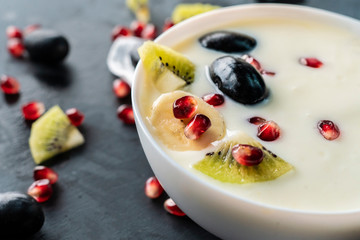 light fresh yogurt in a ceramic bowl with small pieces of tropical fruits, kiwi, banana, garnet, grapess