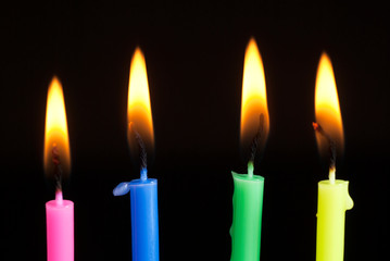 Colorful candles burning in the dark. Flames in darkness.