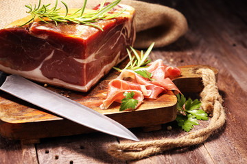 Italian prosciutto crudo or jamon with rosemary. Raw ham on wooden board