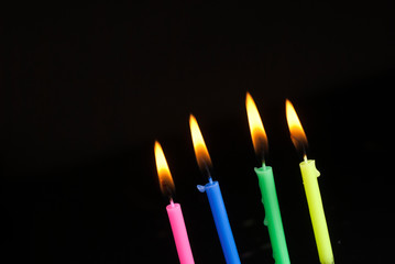 Colorful candles burning in the dark. Flames in darkness.