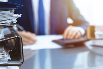 Binders with papers waiting to be processed with businessman or bookkeeper back in blur. Accounting planning budget. Audit, insurance  and business concept