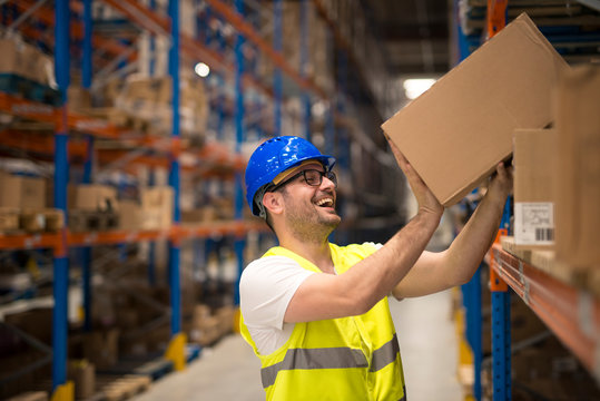 Working at warehouse. Smiling warehouse worker moving boxes on the shelf.