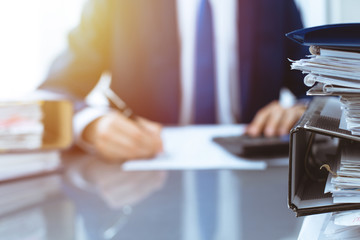 Binders with papers waiting to be processed with businessman or bookkeeper back in blur. Accounting planning budget. Audit, insurance  and business concept
