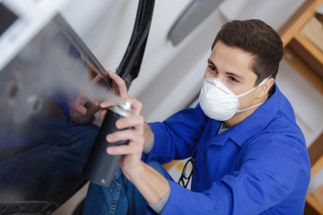 young mechanic respraying car panel