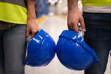 Head protection at work. Close up of two unrecognizable industrial workers holding hardhat protection helmets. Safety equipment at work concept.
