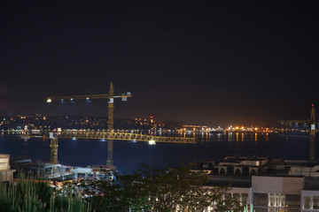 Fototapeta premium View of the construction site against the city lights with reflections on the sea, the maiden's tower and dark sky. Istanbul, Turkey.