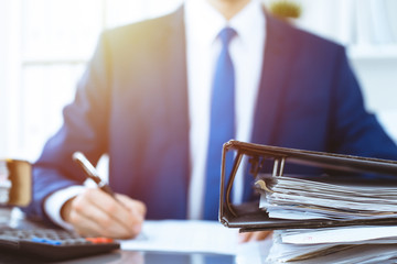 Binders with papers waiting to be processed with businessman or bookkeeper back in blur. Accounting...