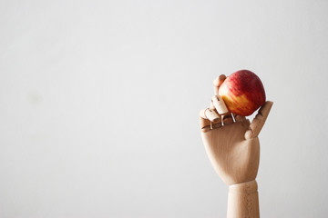 Articulated wood hand holding a red apple on white background - Powered by Adobe